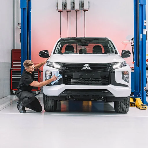 Technician kneeling beside a white Mitsubishi wipping down secondary headlights
